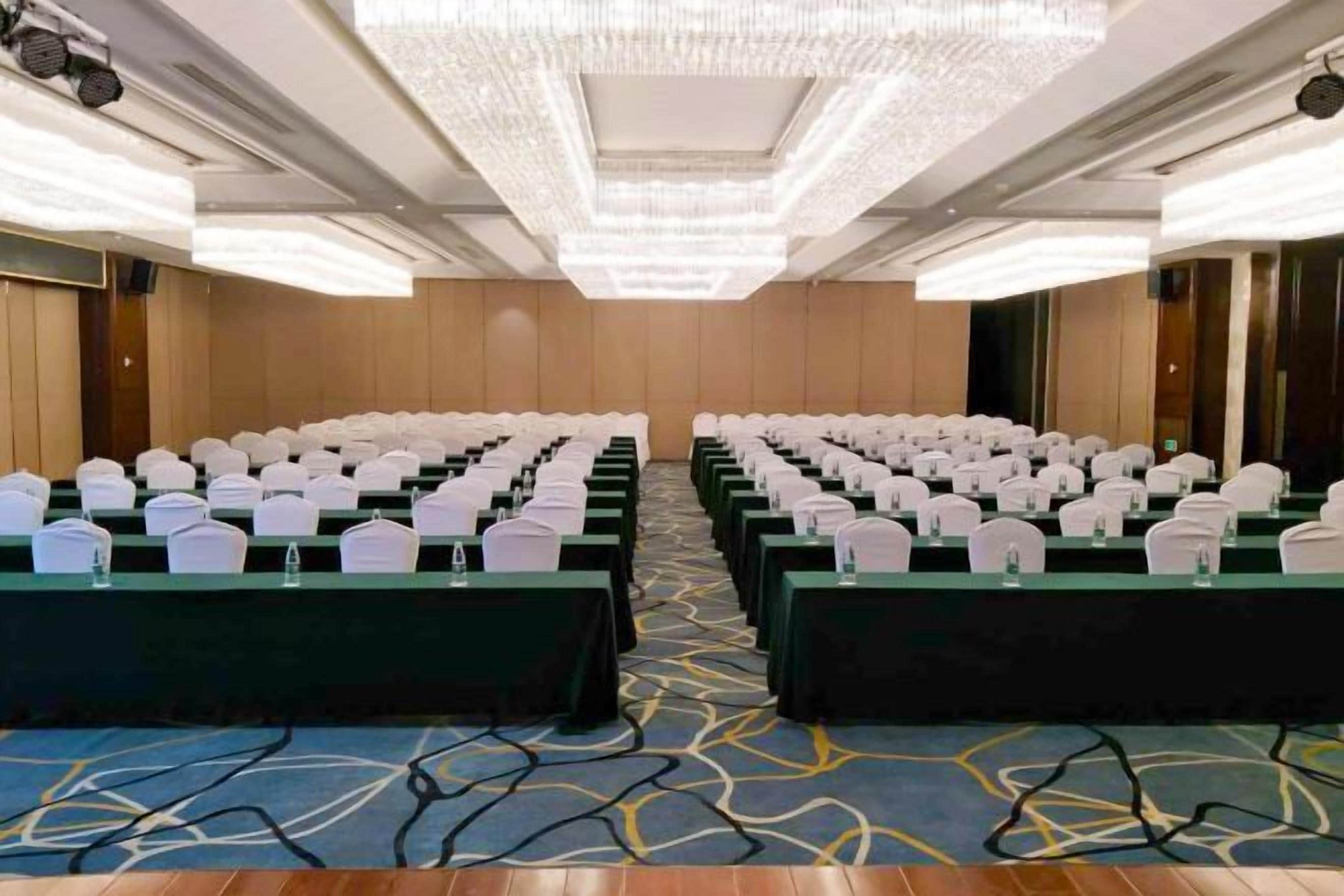 A conference room with rows of tables, each with a white chair and a water bottle.