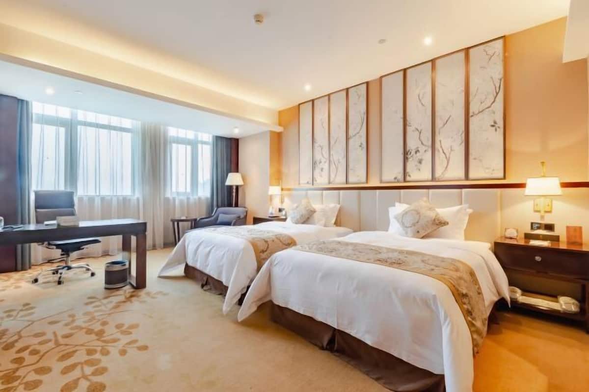 A hotel room with two beds, a desk, a chair, and a large window.