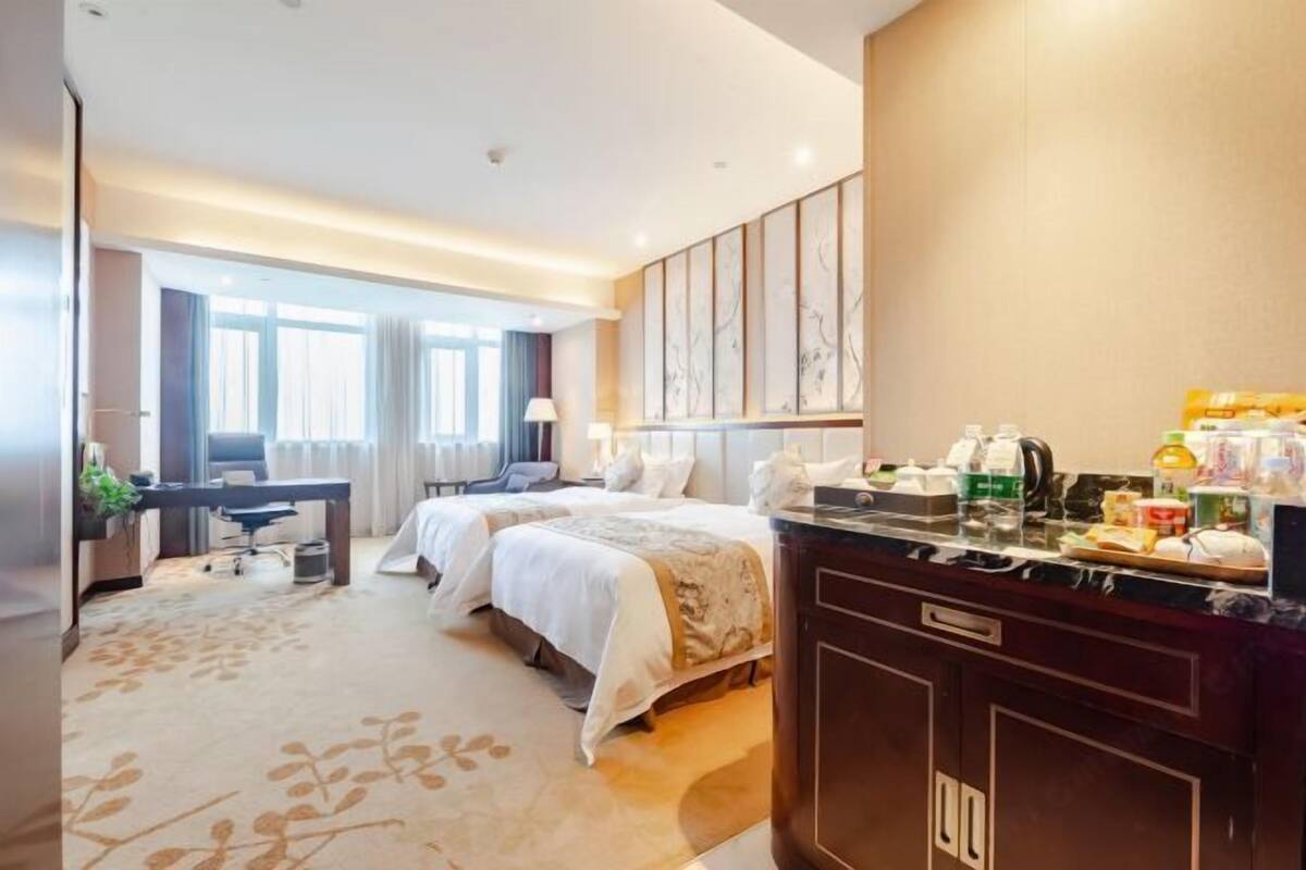 A hotel room with two beds, a desk, and a kitchenette.
