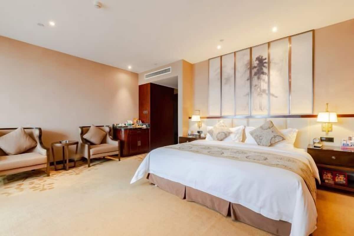 A hotel room with a large bed, two bedside tables, a sofa, and a desk.