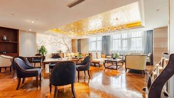 A spacious hotel lobby with a wooden floor, a central dining area, and seating arrangements.