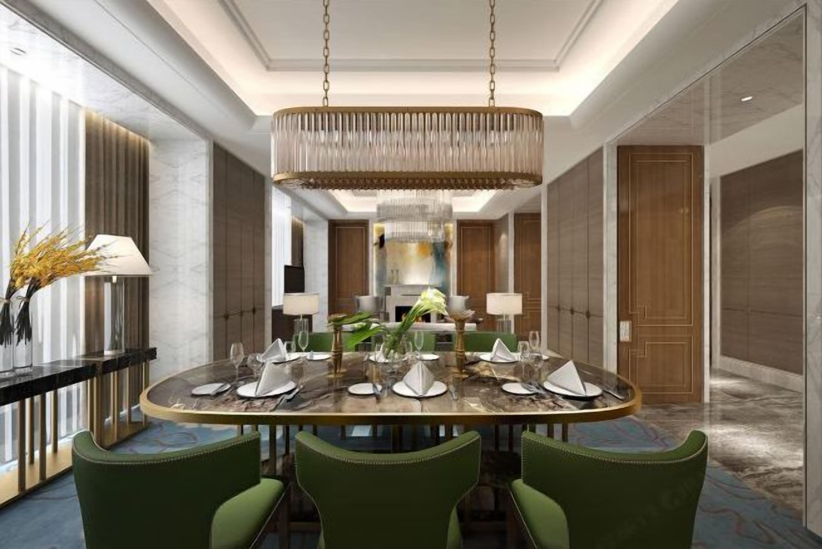 A modern dining area with a round table set for six, surrounded by green upholstered chairs. A large, ornate chandelier hangs from the ceiling, and the room features marble flooring and wood paneling.