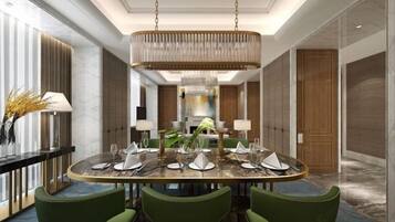 A modern dining area with a round table set for six, surrounded by green upholstered chairs. A large, ornate chandelier hangs from the ceiling, and the room features marble flooring and wood paneling.