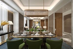 Un comedor moderno con una mesa redonda dispuesta para seis personas, rodeada de sillas tapizadas en verde. Un gran candelabro ornamentado cuelga del techo, y la habitación tiene suelos de mármol y paneles de madera.