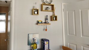 A room with a white door, a framed picture of a guest book, a bottle of wine, and a shelf with various decorative items. - 1st Floor Hillview 2 Bedroomed Central Location (Burnham-on-Sea)
