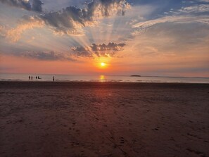 Uma praia com o sol se pondo no horizonte, projetando raios de luz através das nuvens.