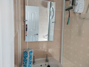 Uma casa de banho com porta branca, espelho, lavatório e chuveiro.