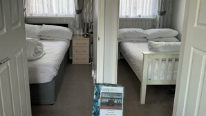 A bedroom with two beds, a bedside table, a nightstand, and a window with curtains. - 1st Floor Hillview 2 Bedroomed Central Location (Burnham-on-Sea)
