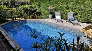 Una piscina rectangular con dos sillas reclinables y una terraza de madera.