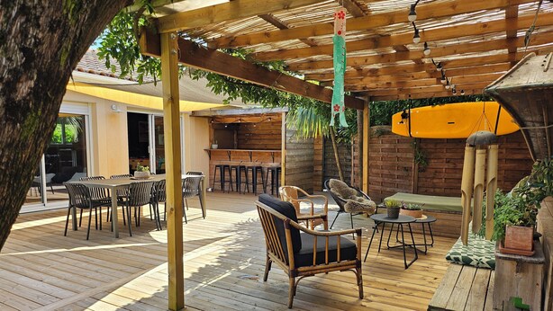 Una terraza de madera con asientos al aire libre, una zona de bar y una sección cubierta con un cascabel colgante.