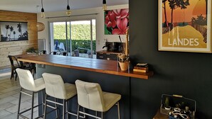 Una cocina moderna con una isla de madera, taburetes de bar, lámparas colgantes y un cuadro grande con un paisaje.