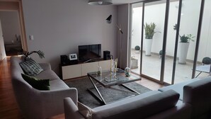 Un salon moderne avec un canapé, une table basse, un téléviseur et un balcon agrémenté de plantes en pot.