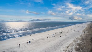 A wide beach with people and umbrellas, a clear sky, and the ocean.