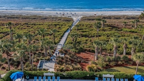 Une station balnéaire dotée d’une promenade pavée menant aux parasols de plage, entourée d’une végétation luxuriante et de palmiers.