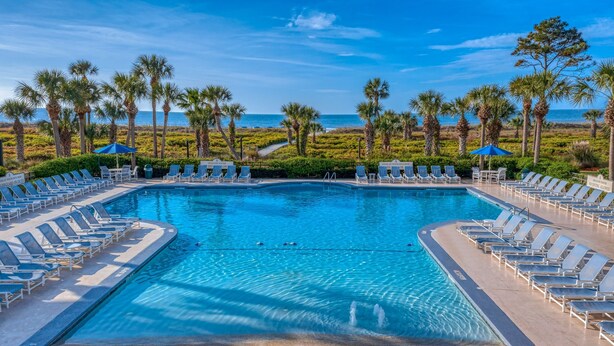 A swimming pool with lounge chairs and palm trees, surrounded by a landscaped area with a view of the ocean.