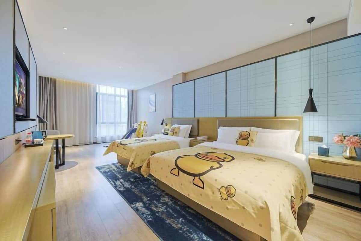Quarto de hotel com duas camas, uma mesa, uma televisão e uma janela grande.
