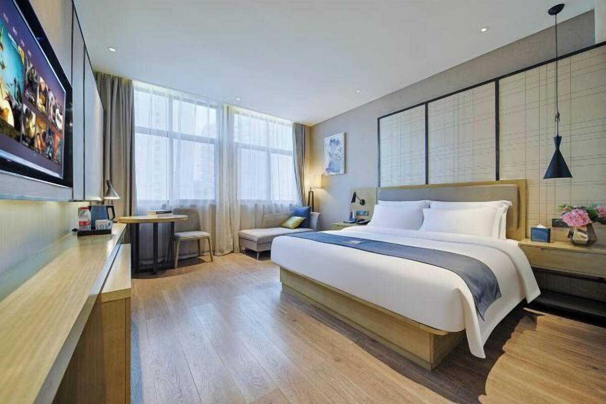 Quarto de hotel moderno com uma cama grande, uma escrivaninha, uma cadeira e uma televisão.