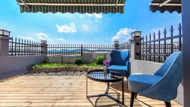 Una terraza de madera con una mesa y sillas, vista a las montañas y una valla metálica.