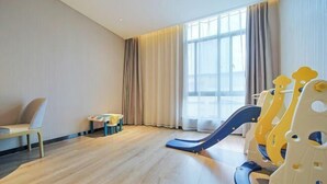 Una habitación con piso de madera, una silla, una mesita y un área de juegos con un tobogán.
