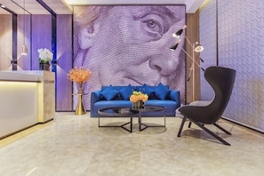 A reception area with a blue sofa, a black chair, a coffee table, and a wall with a large abstract design. - Shangyi Hotel (Qianxi High speed Railway Station Branch) (Qianxi)