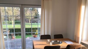Un comedor con una mesa y sillas, un ventanal con cortinas y vistas a un jardín.