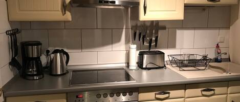 A kitchen with a stainless steel range hood, a coffee maker, a toaster, and a sink with a dish rack.