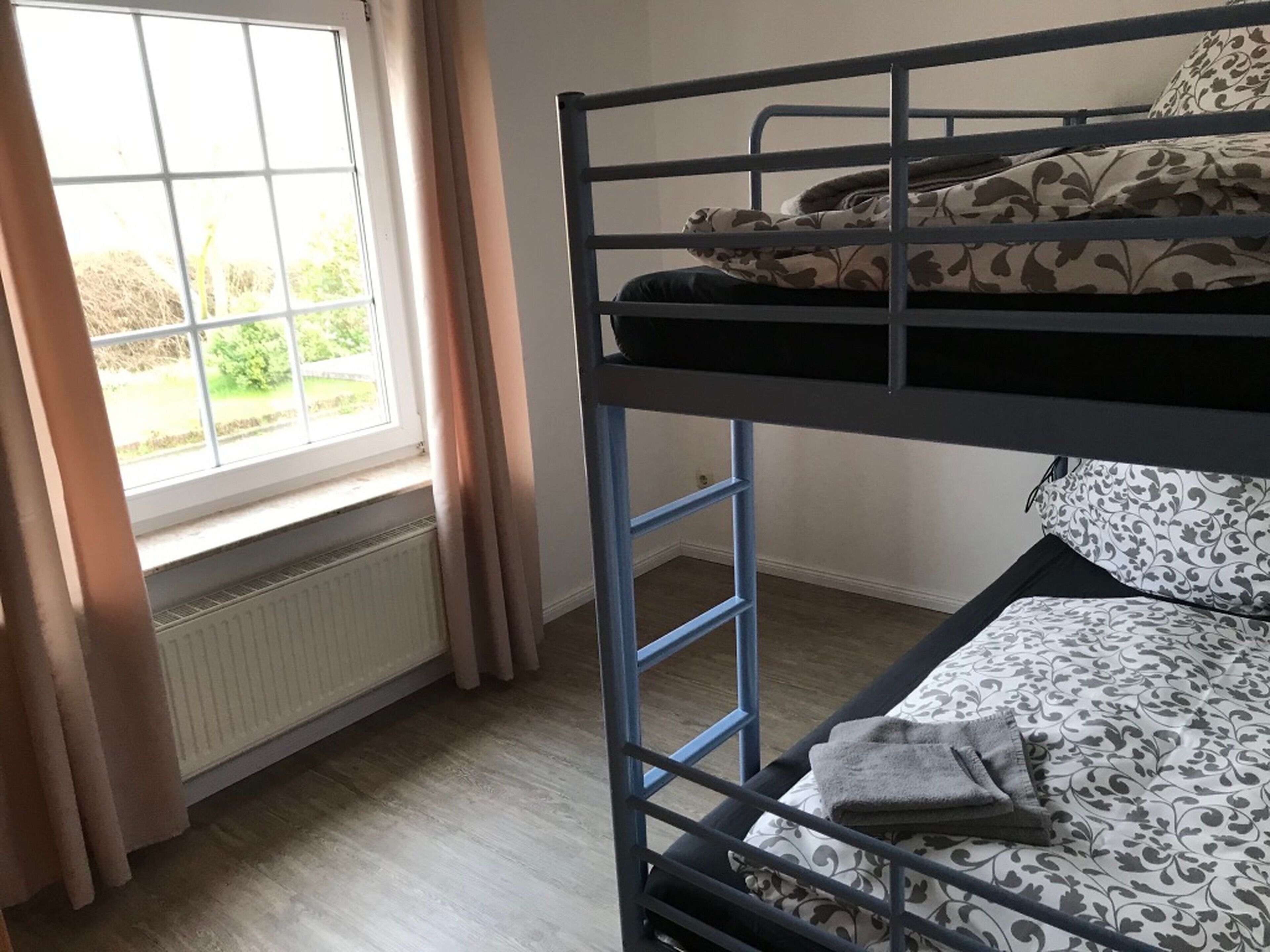 A bunk bed room with a window, curtains, and a radiator.