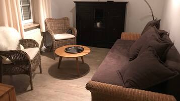 Una sala de estar con muebles de mimbre, un sofá marrón, una mesita redonda y un televisor montado en la pared.