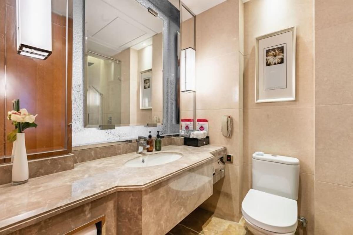 A modern bathroom with a marble sink, a large mirror, a toilet, and a framed picture on the wall.