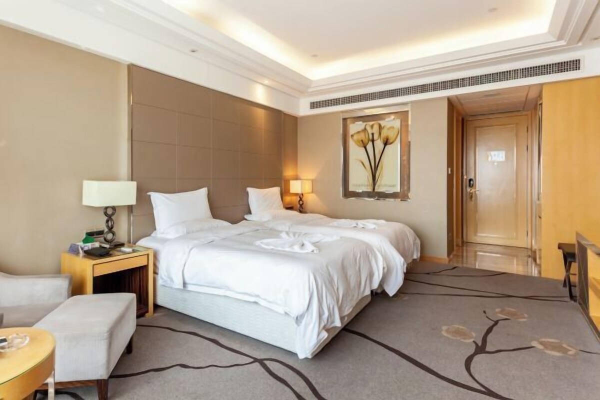 A hotel room with a large bed, a bedside table with a lamp, a chair, and a painting on the wall.