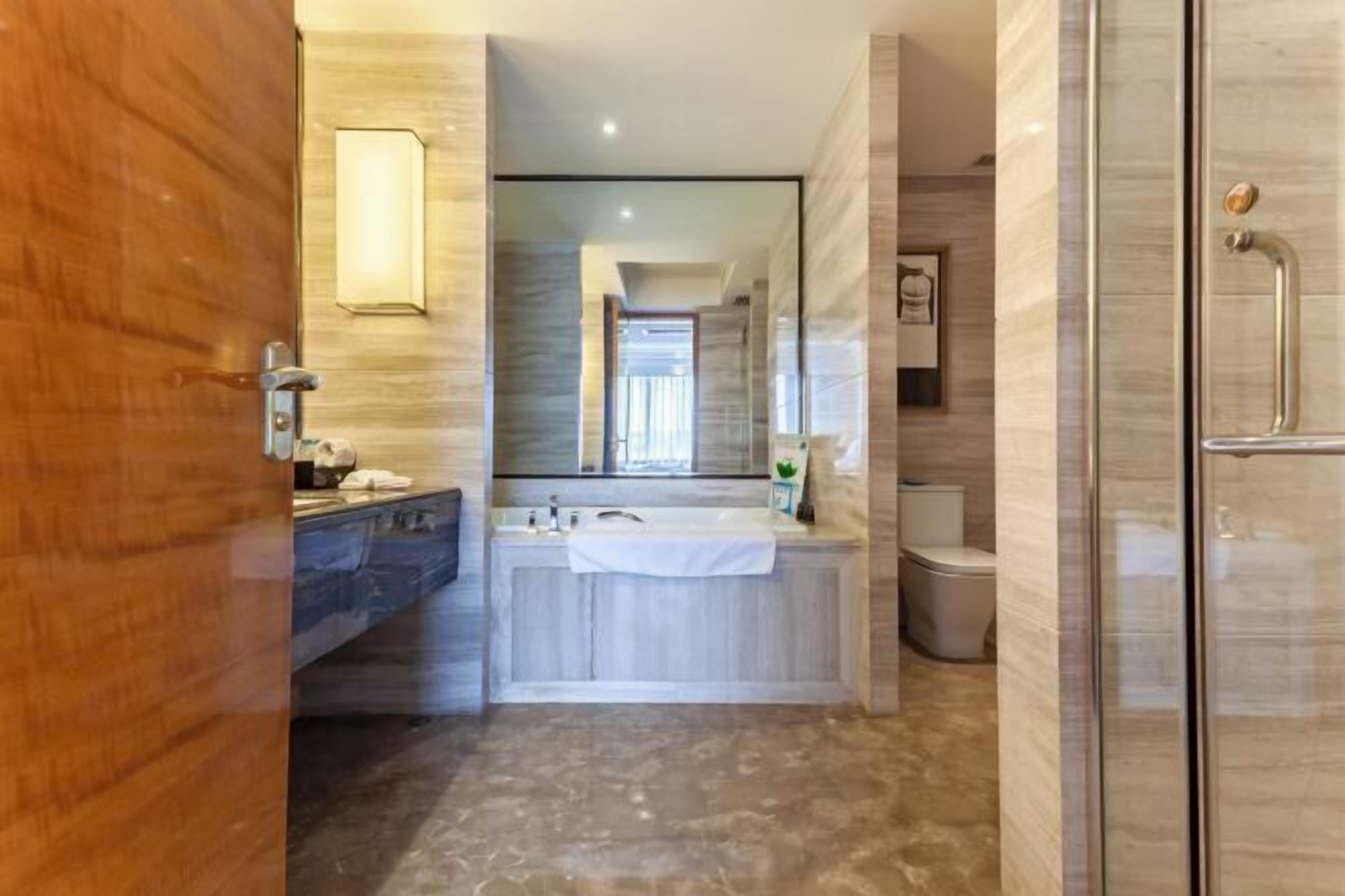 Un baño moderno con puerta de madera, un espejo grande, una bañera, una ducha y un inodoro.