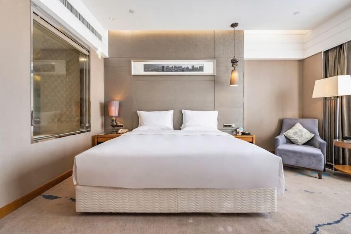 A hotel room with a large bed, a chair, a nightstand, a lamp, and a framed picture on the wall.