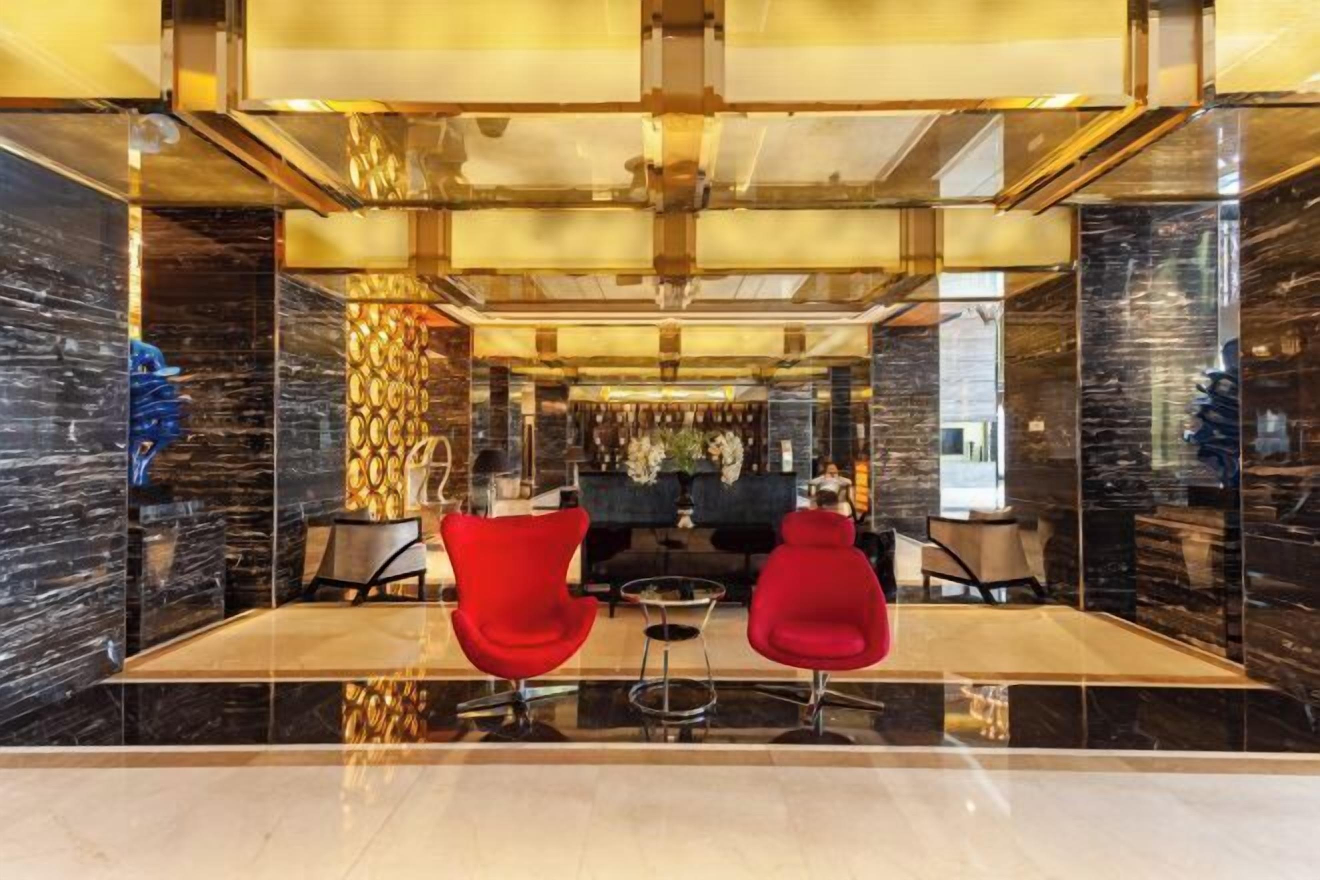 A modern lobby with a glass ceiling, marble walls, and red chairs.