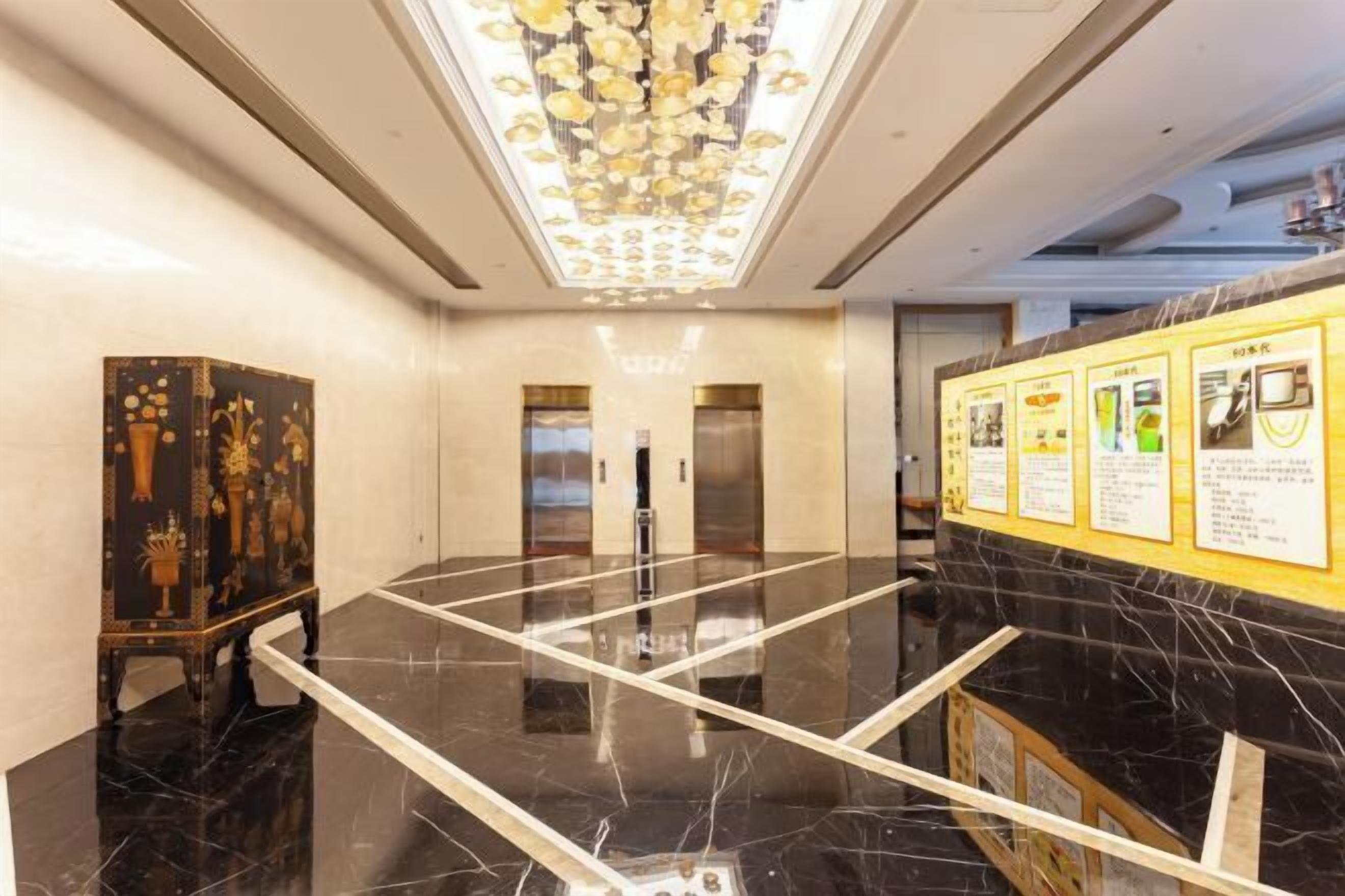 A hotel lobby with a marble floor, a decorative cabinet, an elevator, and informational posters on the wall.