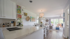 Una cocina moderna con armarios blancos, encimera de mármol y un comedor con mesa y sillas blancas.