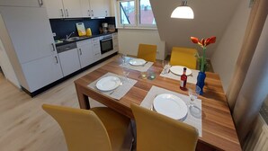 Uma cozinha moderna com armários brancos, uma mesa de jantar posta com pratos, copos e um vaso com flores.