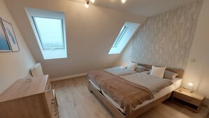 Quarto com uma cama grande, duas mesas de cabeceira, um aparador de madeira e dois claraboias.