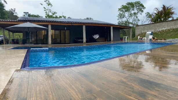 Une piscine avec une terrasse en bois, un espace salon couvert et un bâtiment doté d’un toit en tuiles.