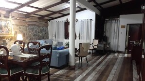 Un comedor con pared de piedra, una mesa de madera y sillas. Hay un salón con un sofá y una lámpara.