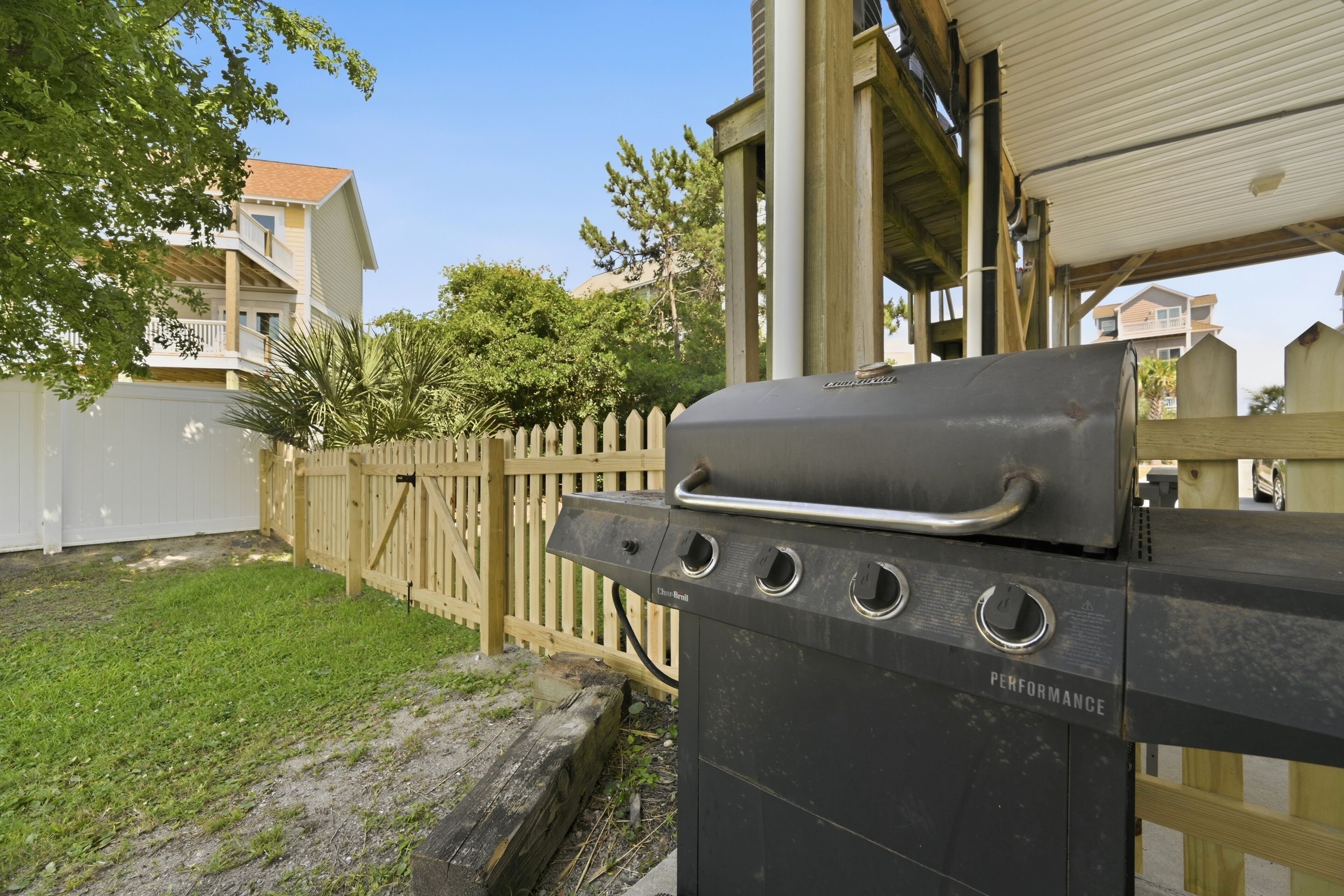 A barbecue grill labeled 'Performance' in a backyard with a wooden fence, a white building, and a clear sky.
