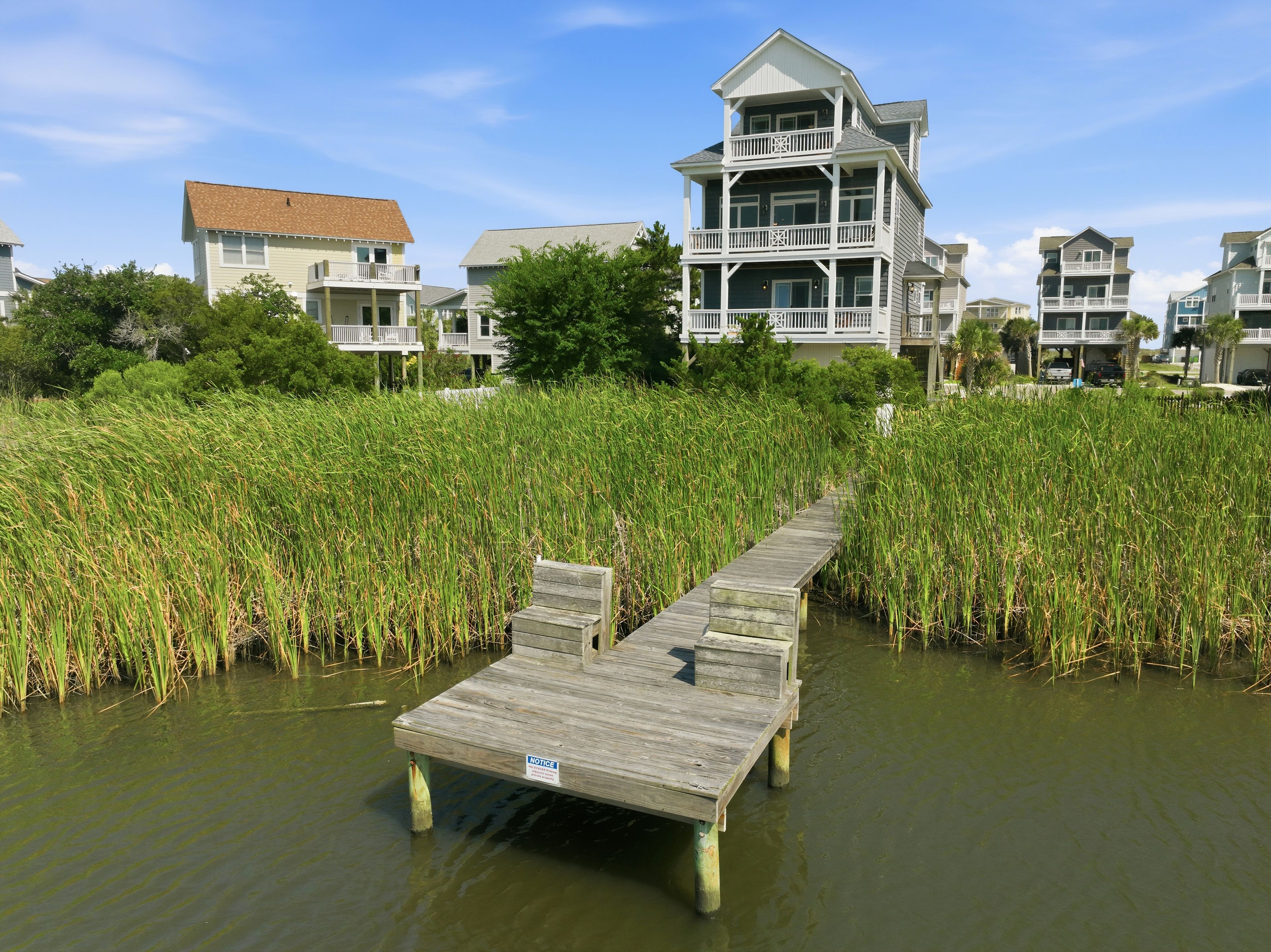 A wooden dock leading to a house with a balcony, surrounded by tall grass.