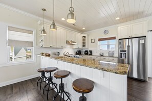 Een keuken met witte kasten, een granieten aanrecht, roestvrijstalen apparatuur, hanglampen en een groot eiland met krukken.