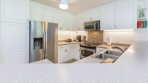 A modern kitchen with white cabinets, stainless steel appliances, a microwave, a toaster, and a sink. - Hawaii Life Rental Presents Emmalani 423 (Princeville)