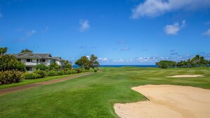 A golf course with a house on the left, a clear sky, and a view of the ocean. - Hawaii Life Rental Presents Emmalani 423 (Princeville)