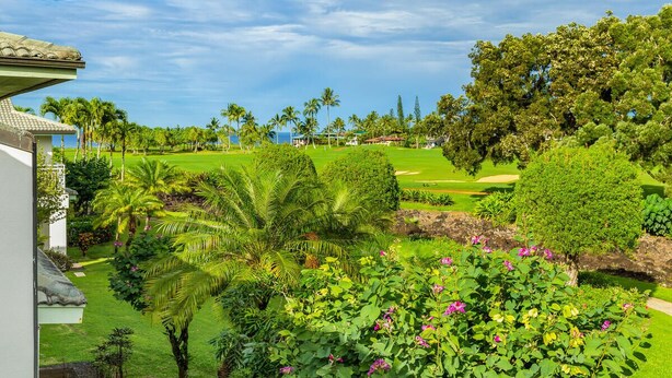 A lush garden with palm trees, a golf course, and a view of the ocean. - Hawaii Life Rental Presents Emmalani 423 (Princeville)