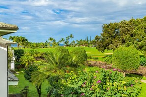 A lush garden with palm trees, a golf course, and a view of the ocean. - Hawaii Life Rental Presents Emmalani 423 (Princeville)