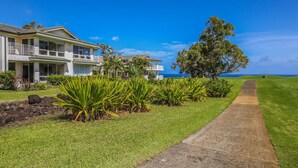 A beachfront property with a large house, a paved walkway, and lush greenery. - Hawaii Life Rental Presents Emmalani 423 (Princeville)