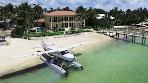 Une maison située au bord de la plage, offrant une vue dégagée sur un hydravion sur l’eau.