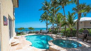 Une piscine avec un jacuzzi, entourée de palmiers et offrant une vue sur l’océan.