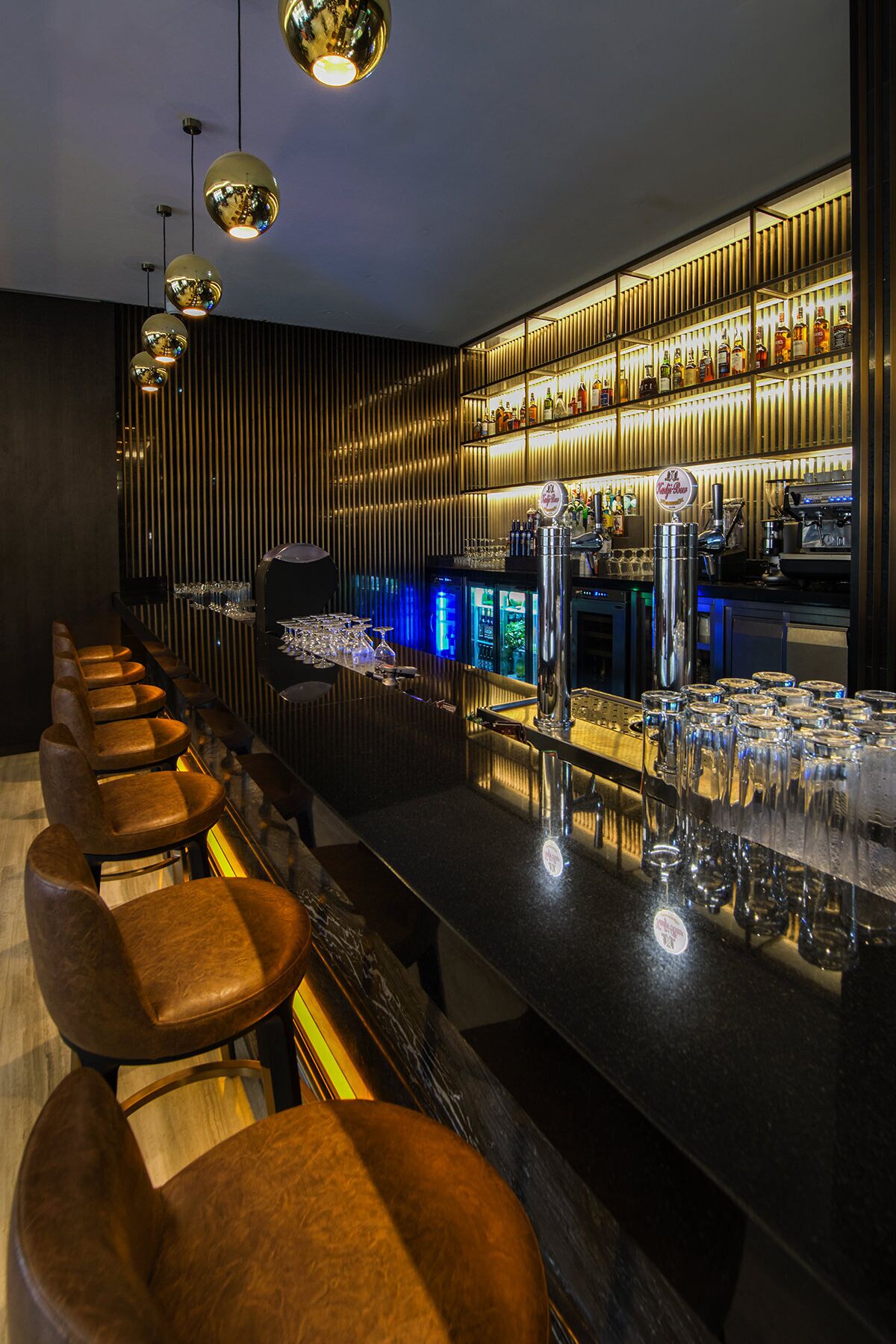 A bar area with a long counter, multiple stools, and a well-stocked shelf with various bottles.